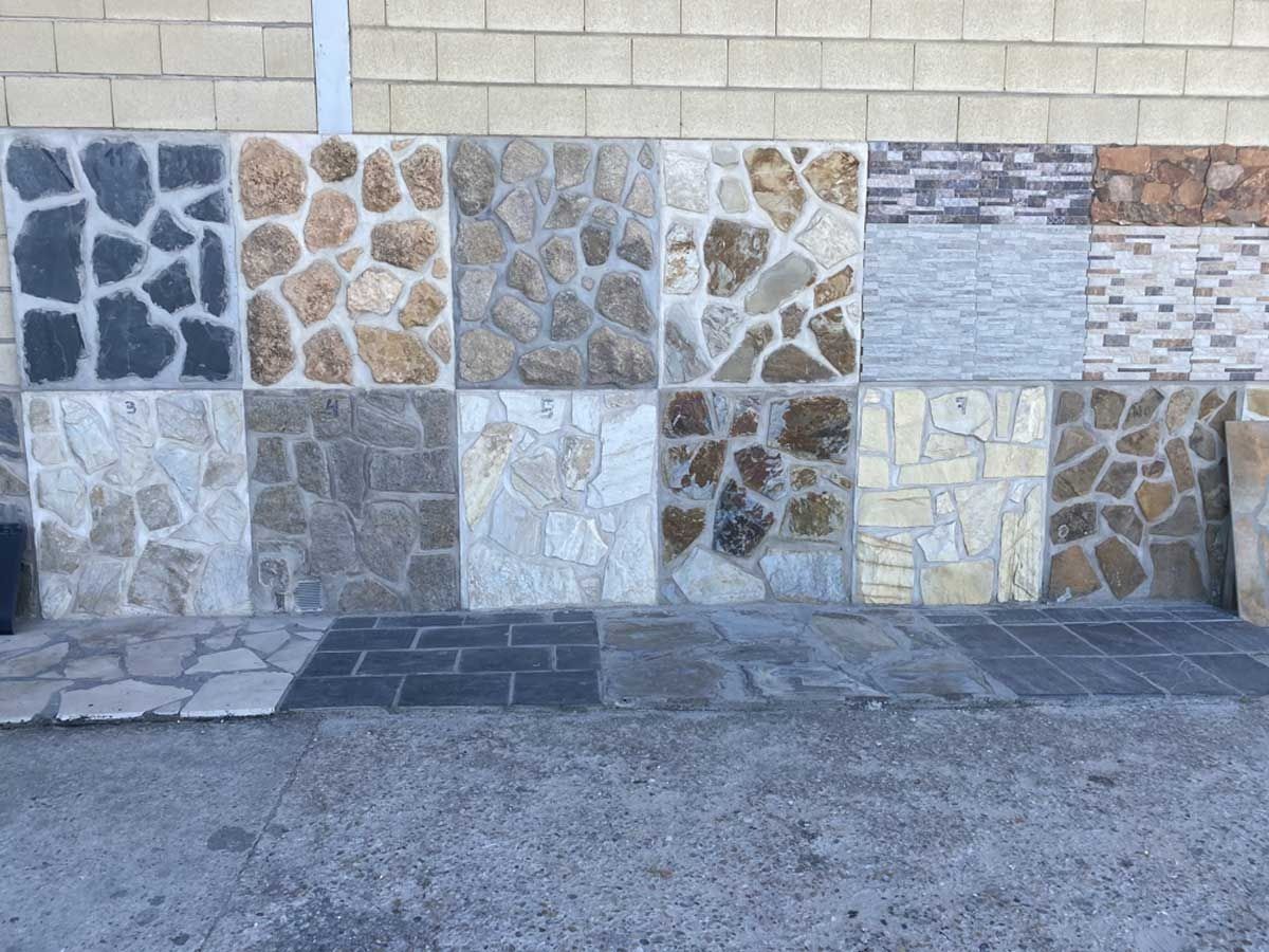 Un revestimiento de pared y suelo con diversos diseños de baldosas cuadradas de piedra en tonos grises, beige, marrones y blancos.