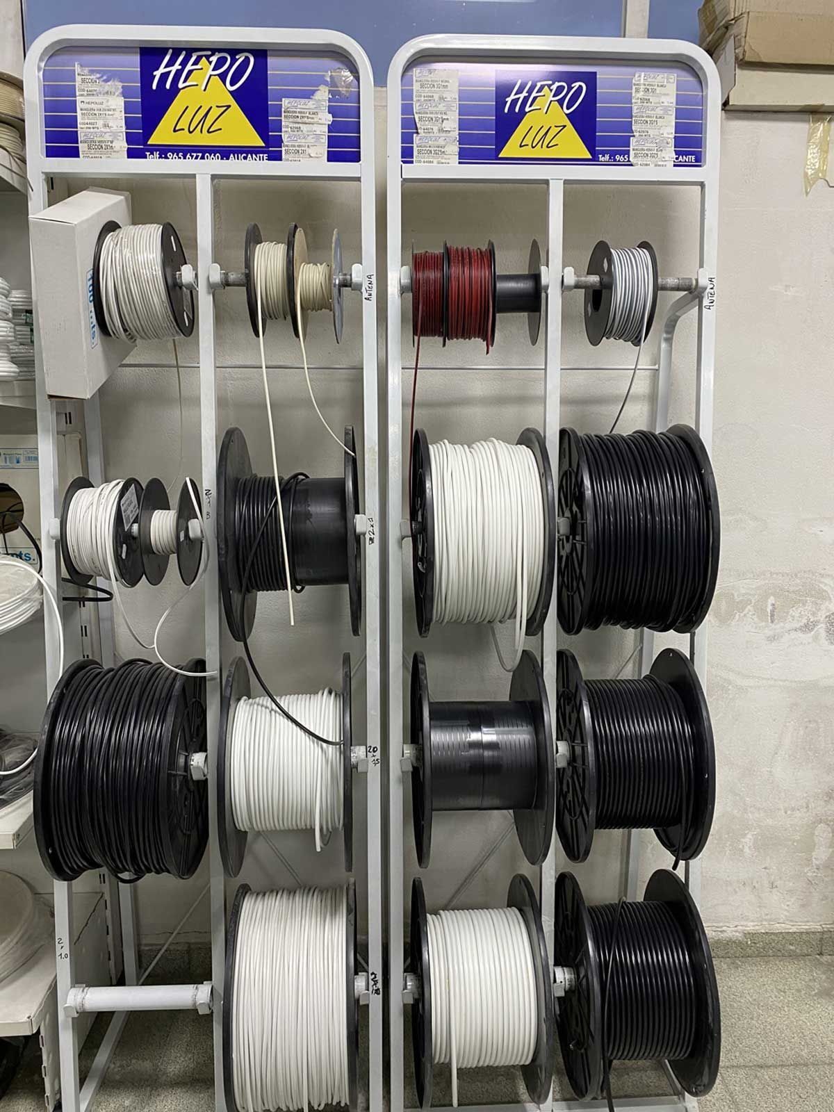 Dos expositores verticales para comercios que contienen varias bobinas de cables eléctricos de diferentes colores: negro, blanco y rojo.