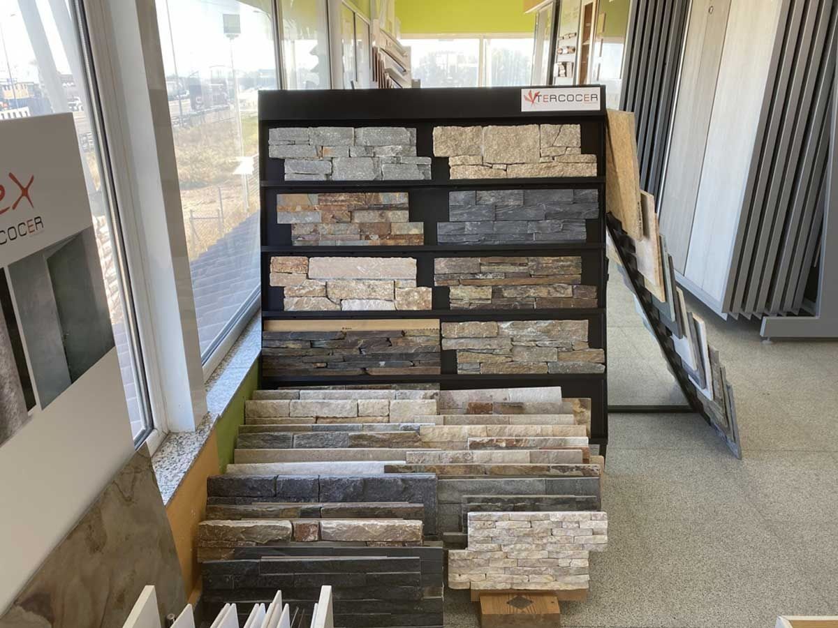 Un expositor en una tienda que muestra diversas muestras de baldosas de piedra apilada en tonos grises, beige y tostados.