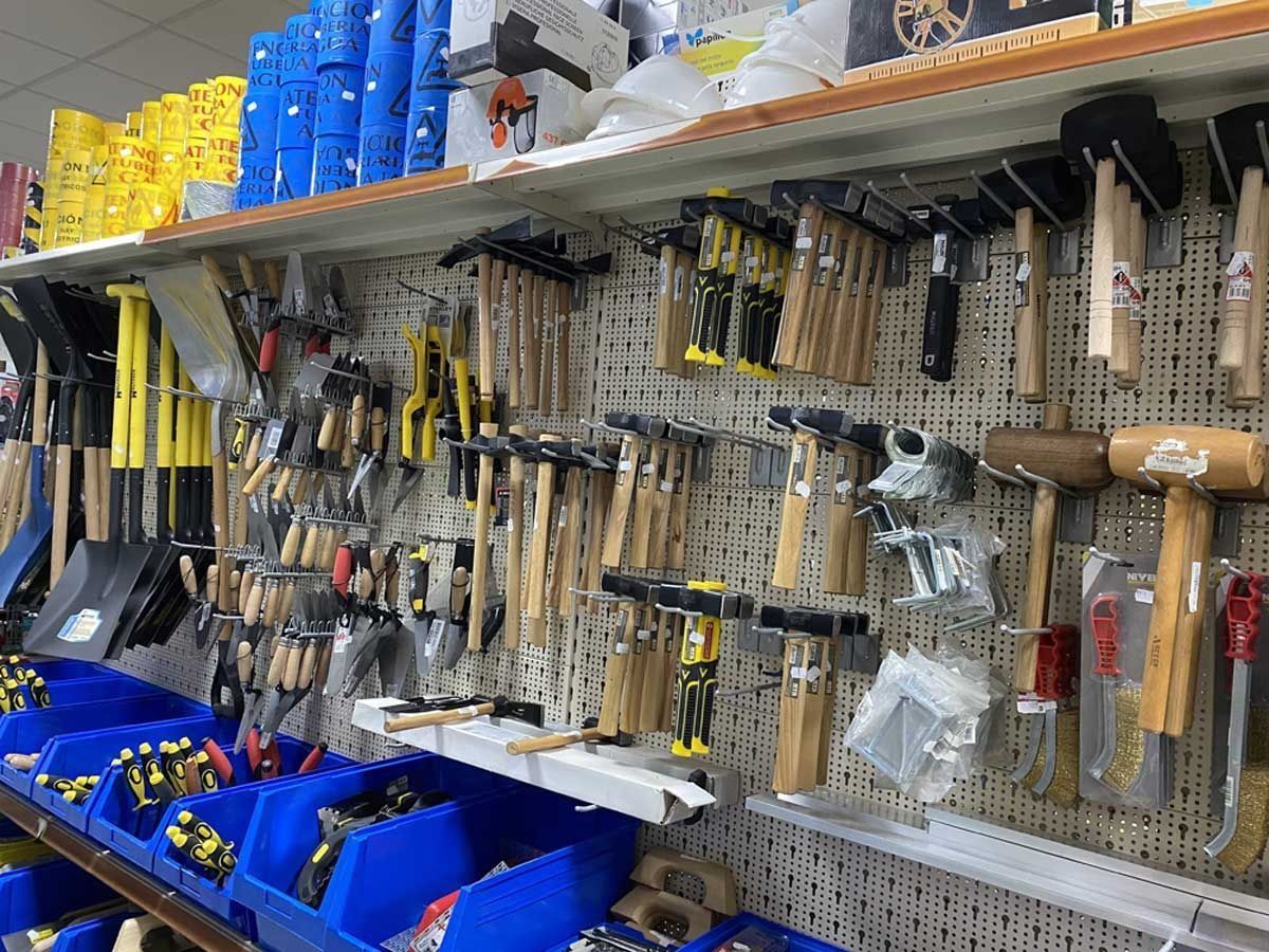 Estantería de una tienda que exhibe una variedad de martillos, mazos y herramientas colgadas en un panel perforado con contenedores azules debajo.