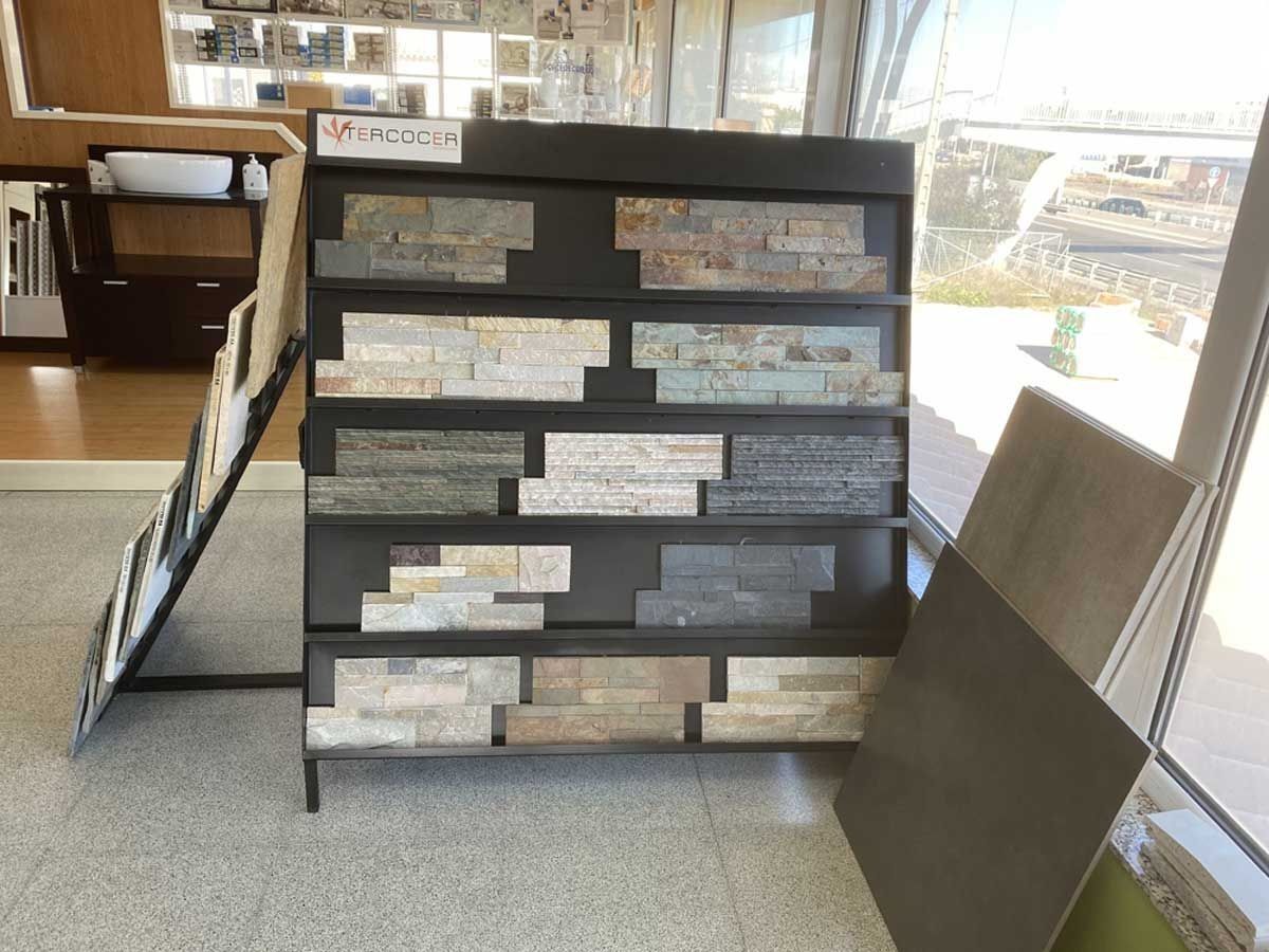 Un expositor en la sala de exposición de una tienda que muestra varias muestras de azulejos de pared de piedra apilada en tonos tierra.