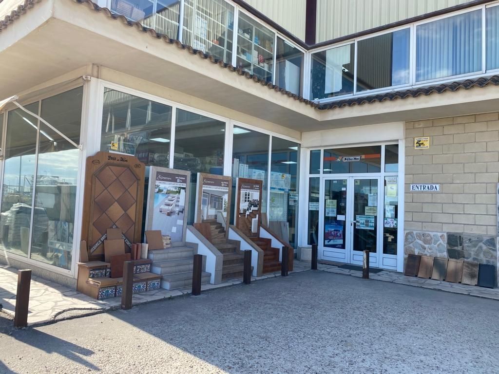 Un escaparate con escaleras revestidas de azulejos y diversas muestras de piedra, situado bajo un edificio con balcones de cristal.