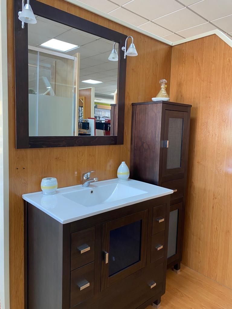 Mueble de baño de madera oscura con lavabo blanco, espejo a juego y armario alto para almacenamiento, sobre paredes de madera clara.