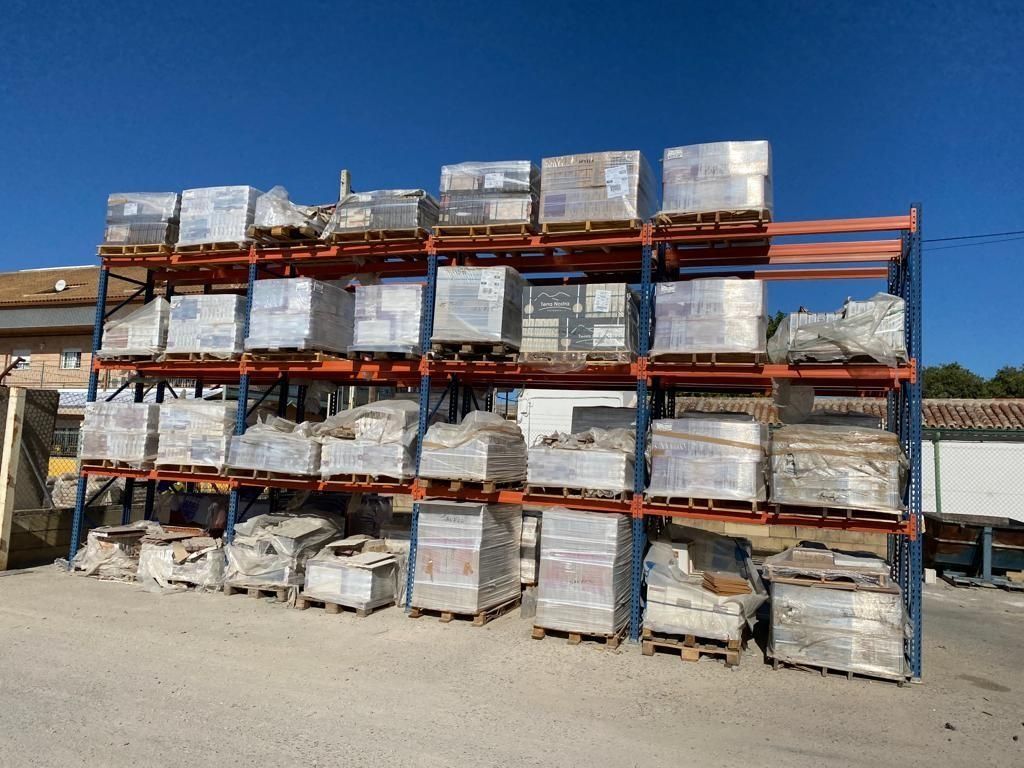 Estanterías para palés almacenadas al aire libre, repletas de pilas de materiales de construcción envueltos bajo un cielo azul despejado.