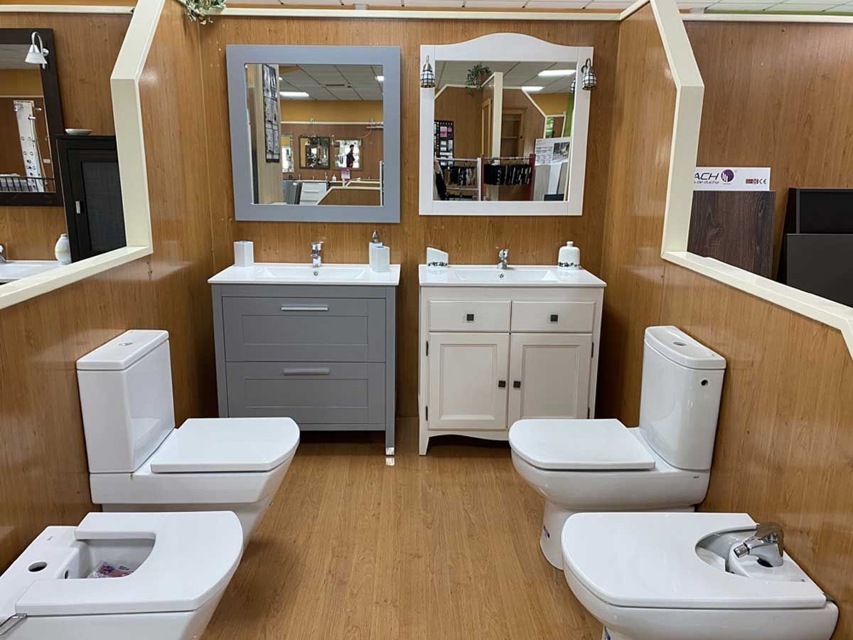 Dos conjuntos de tocador para baño con lavabos, espejos, inodoros y bidés se exhiben en una sala de exposición con paredes revestidas de madera.