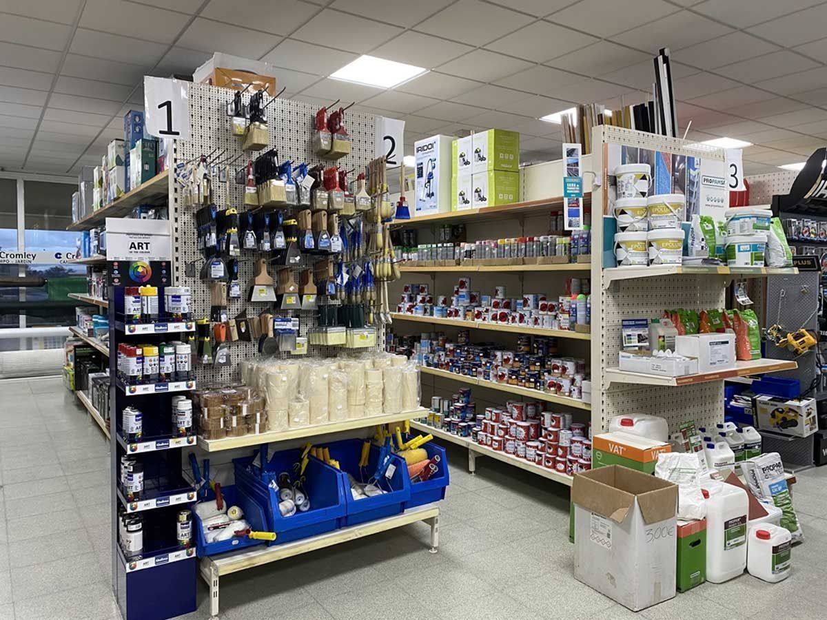 Estanterías en una ferretería repletas de pinceles, herramientas y recipientes con suministros.