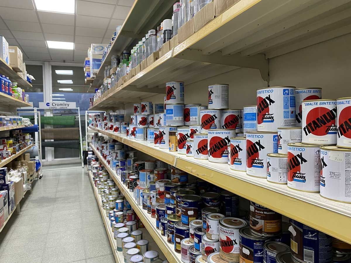 Estanterías repletas de latas de pintura y artículos de ferretería en un pasillo de una tienda.