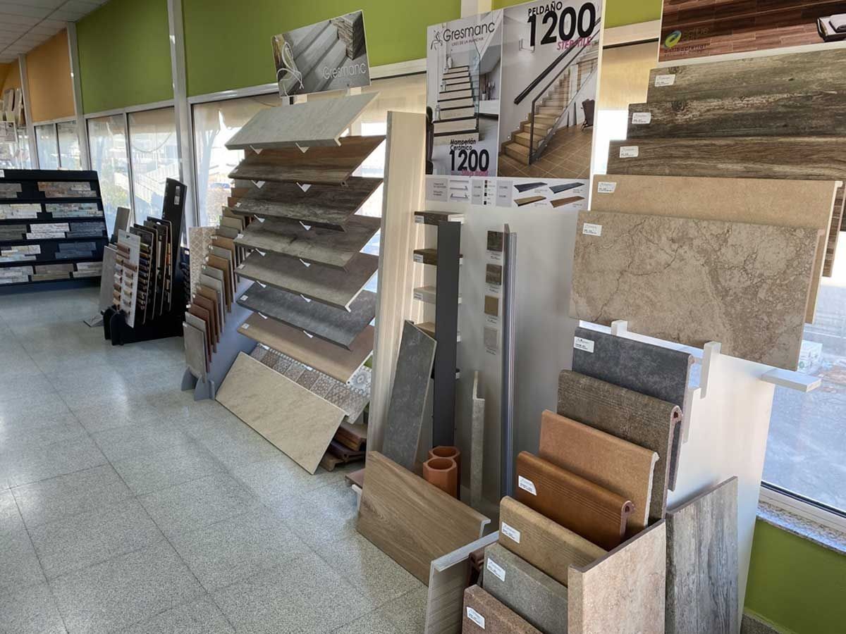 En una sala de exposición de azulejos y suelos se muestran muestras de peldaños y tablones de suelo con aspecto de madera, piedra y cerámica, expuestas en estanterías.