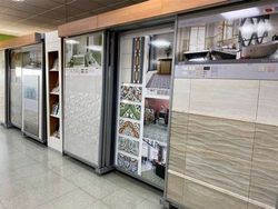 Un expositor en sala de muestras que presenta diversos azulejos de pared de gran tamaño, incluyendo diseños decorativos y losas texturizadas de color beige.