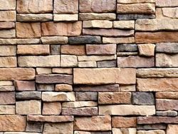 Muro de piedra apilada con rocas rectangulares de tonos tierra, en tonalidades beige, marrón y gris.