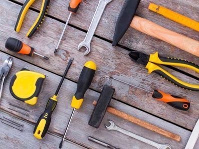 Diversas herramientas, entre ellas destornilladores, alicates, martillos y una cinta métrica, dispuestas sobre una superficie de madera desgastada.