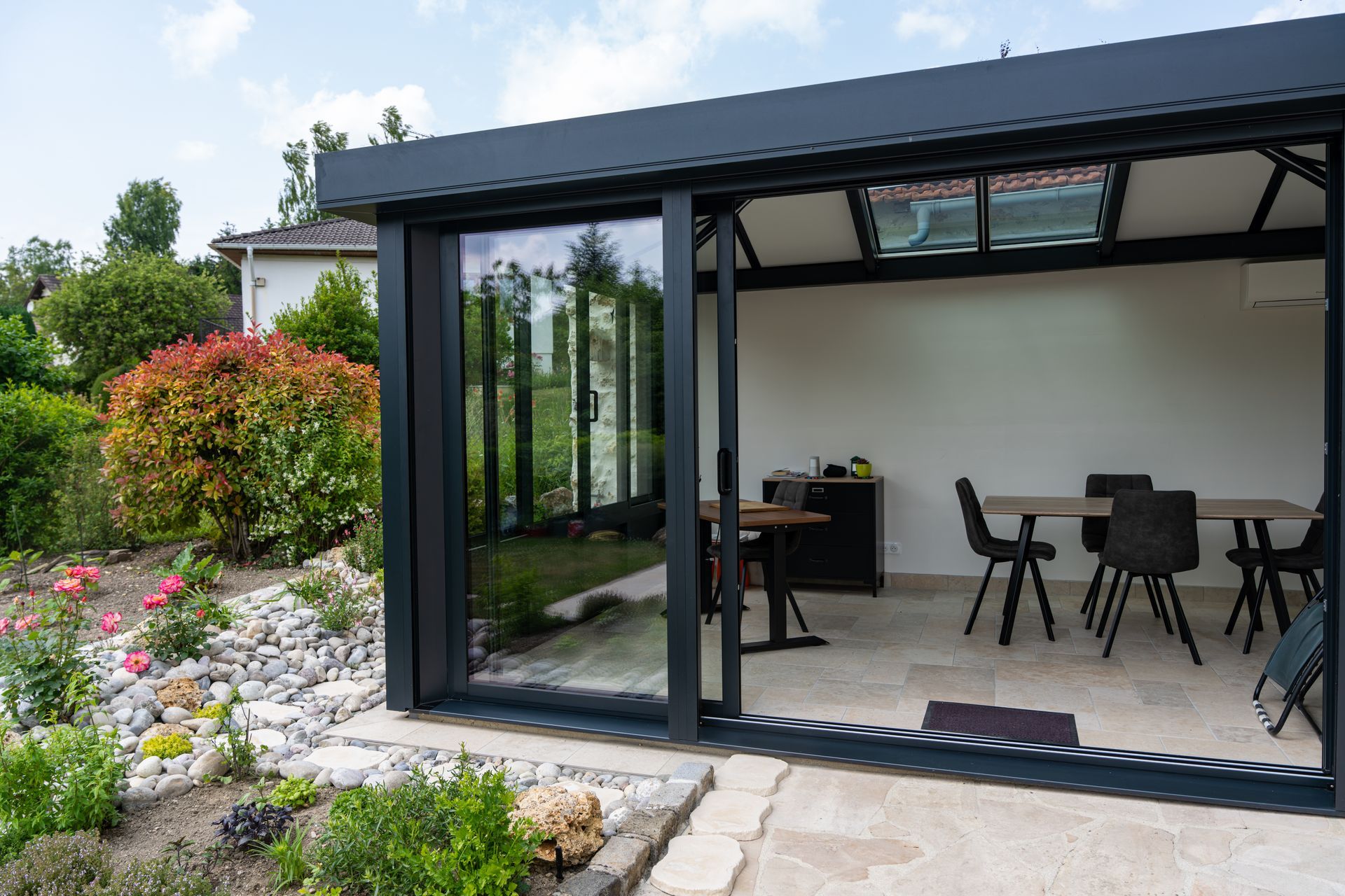 Patio moderne avec parois vitrées à cadre noir, table et chaises de salle à manger, donnant sur un jardin paysager