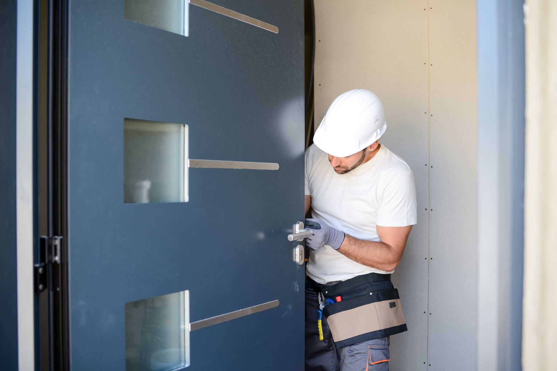Un ouvrier installe une serrure sur une porte bleue à l'intérieur d'une entrée.