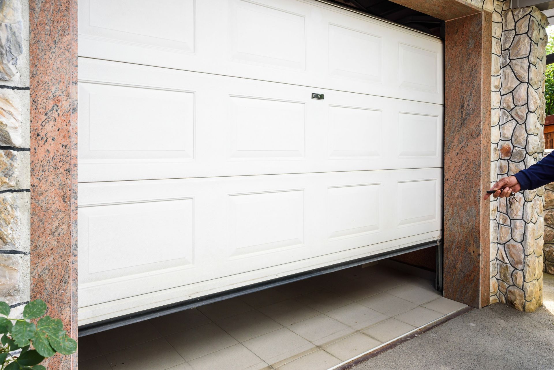 Porte de garage blanche entrouverte, une main est posée sur le bord droit.