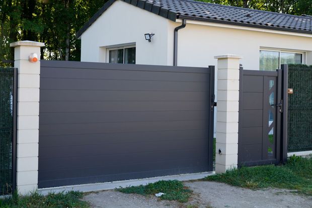 Entrée de maison moderne avec portail coulissant gris foncé et piliers blancs