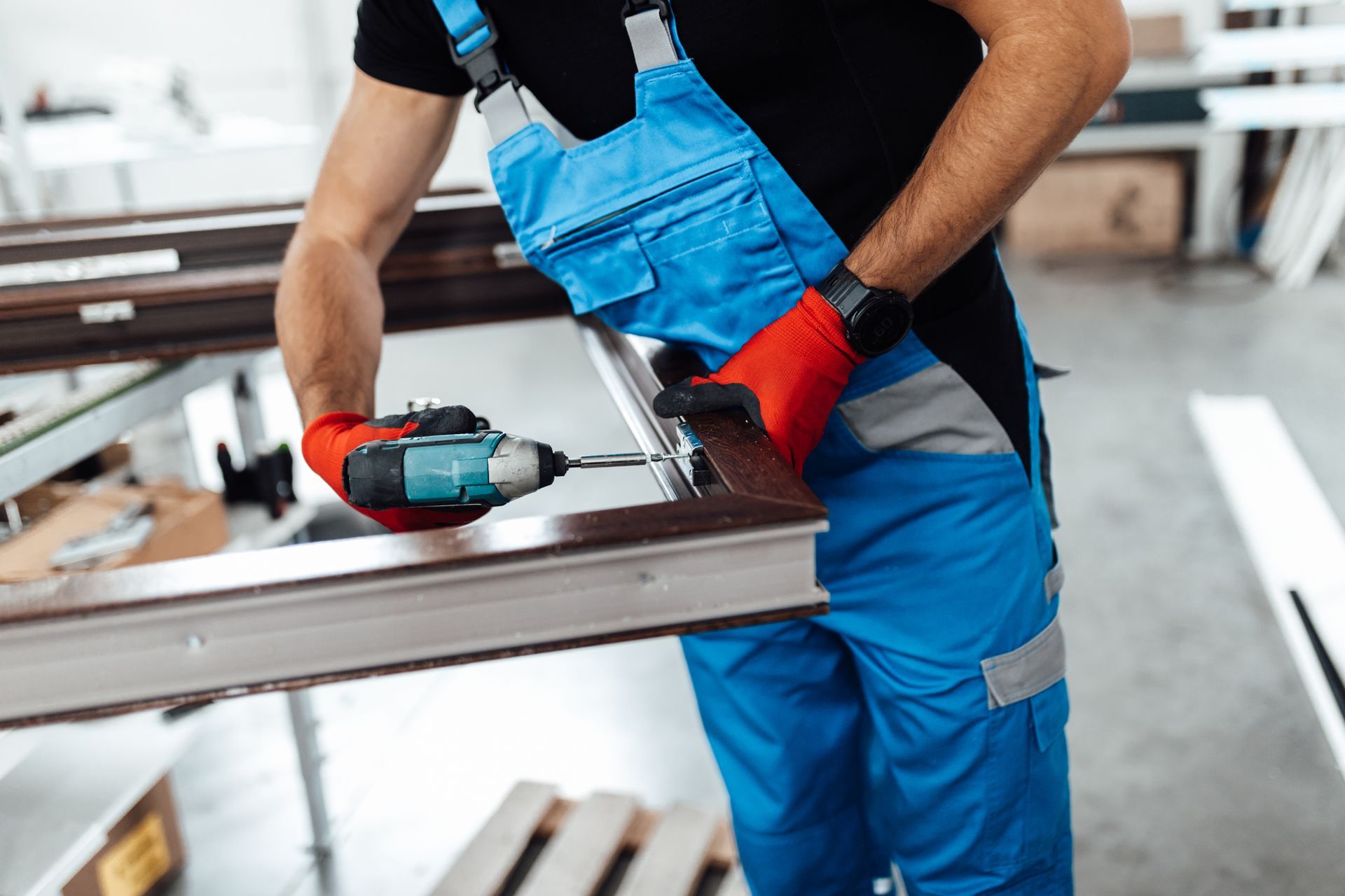 Ouvrier en salopette bleue utilisant une perceuse électrique sur une structure métallique dans un atelier