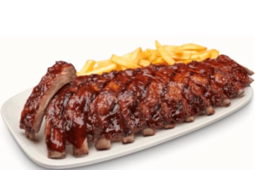 Un plato blanco cubierto con costillas y papas fritas.