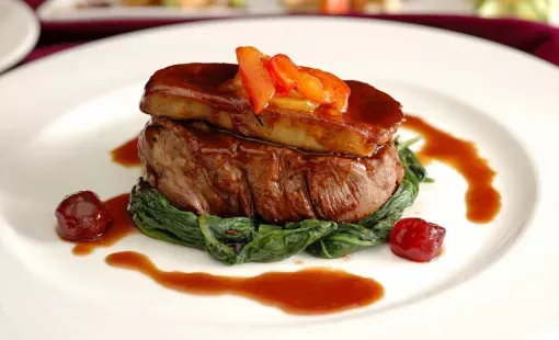Steak saisi accompagné d’épinards et de carottes glacées, nappé de sauce brune, servi dans une assiette blanche