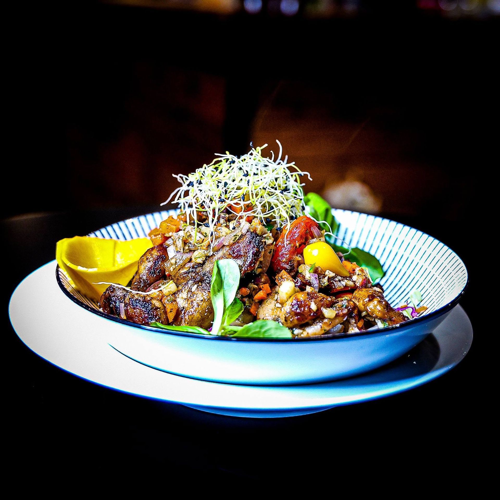 Plat gastronomique dressé avec de la viande grillée, des pousses, des herbes aromatiques et des quartiers de citron