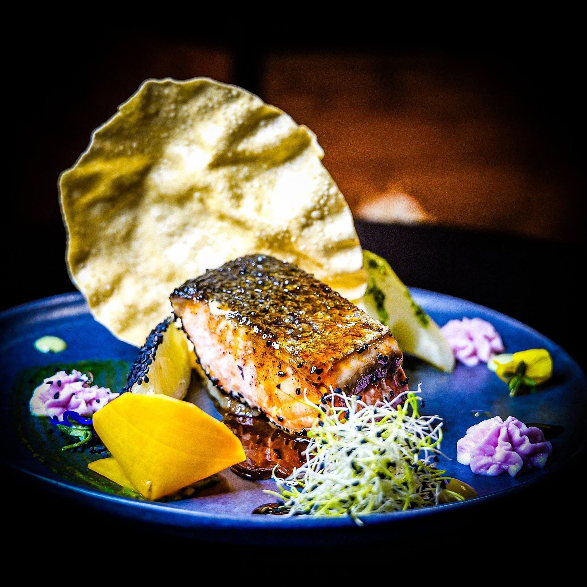 Filet de saumon gastronomique sur une assiette bleue, accompagné d’une gaufrette croustillante et de micropousses