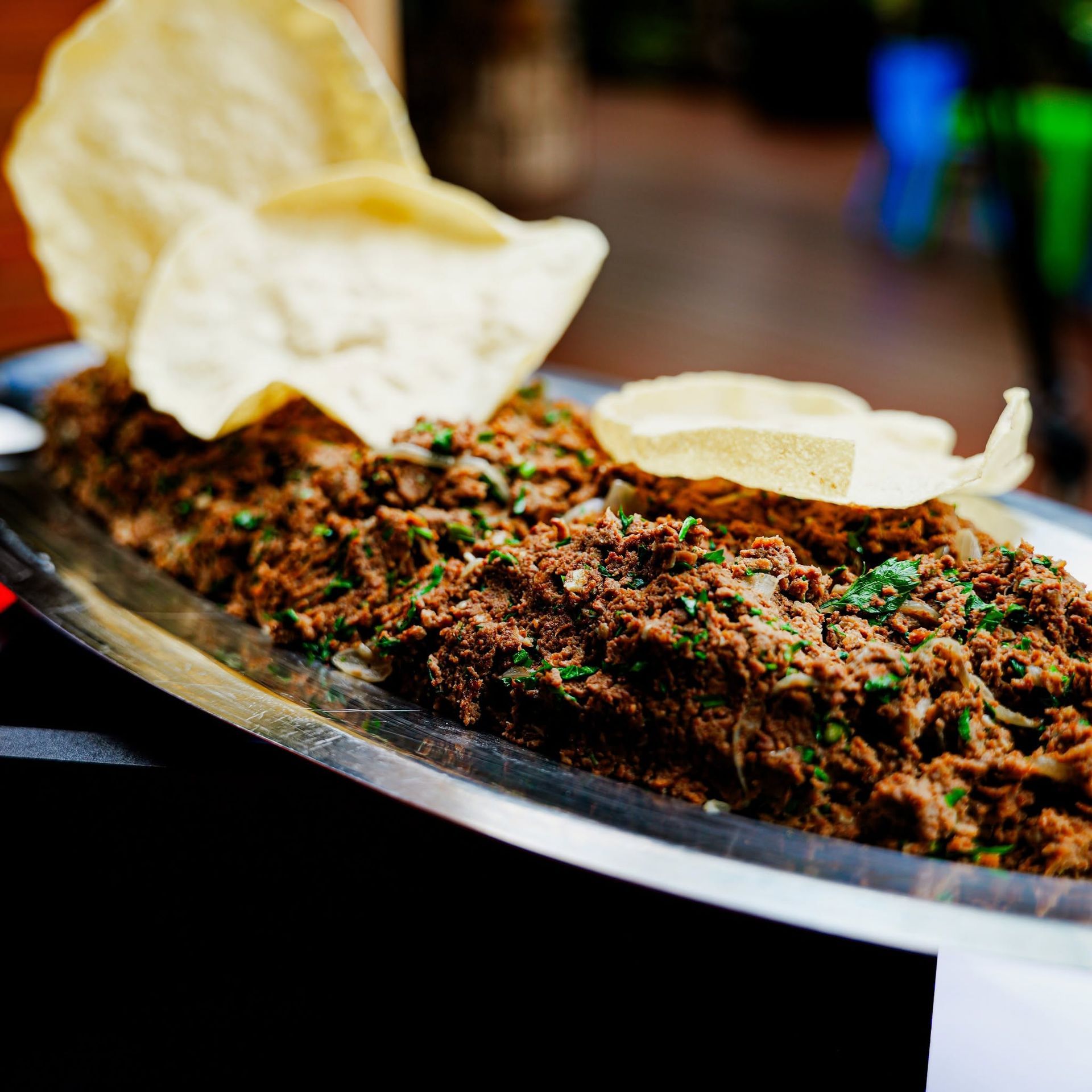 Viande hachée épicée sur un plateau de service, accompagnée de papadums et de quartiers de citron