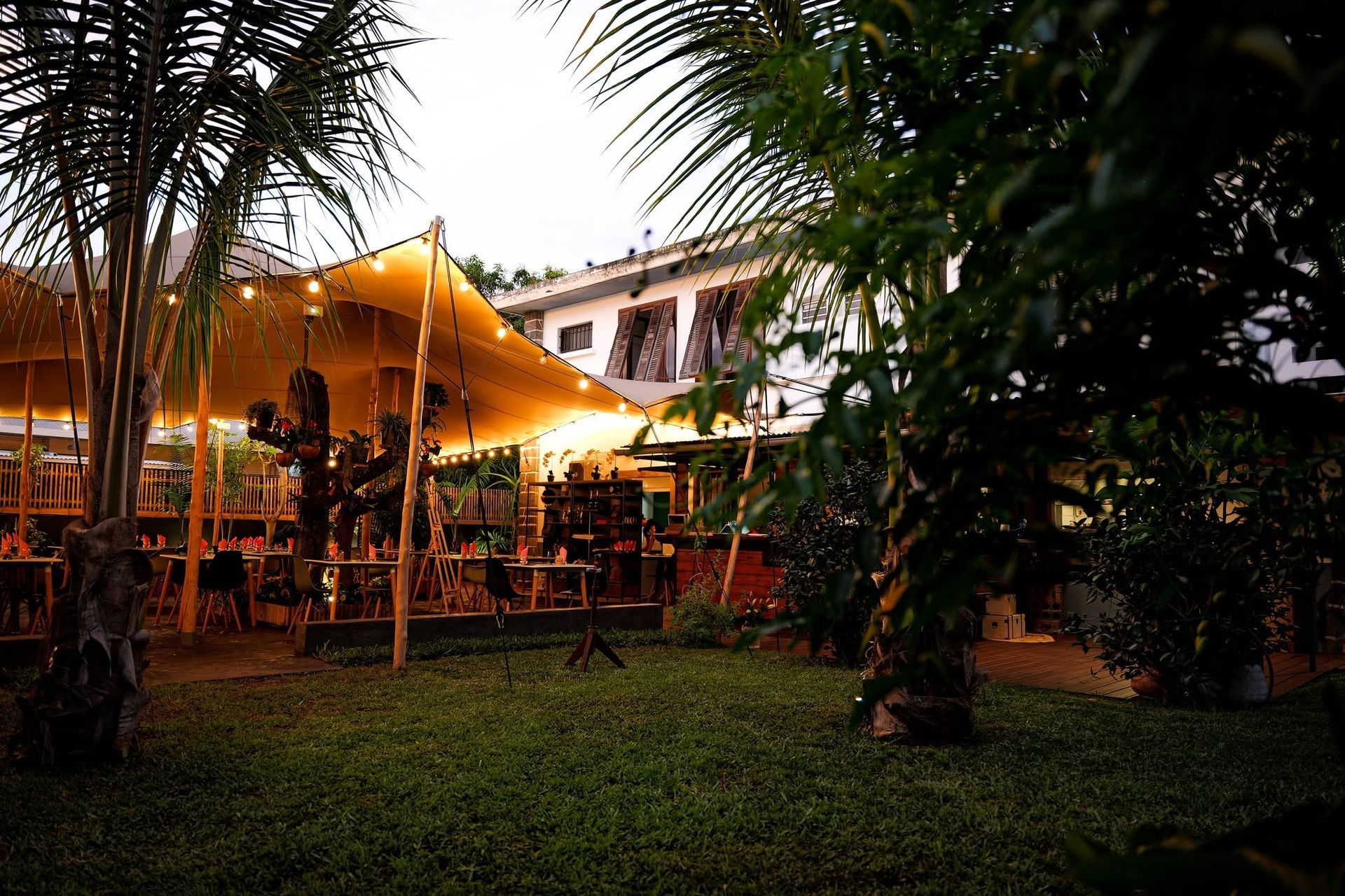 Restaurant en plein air avec une toile jaune chaleureuse et des tables entourées de verdure au crépuscule