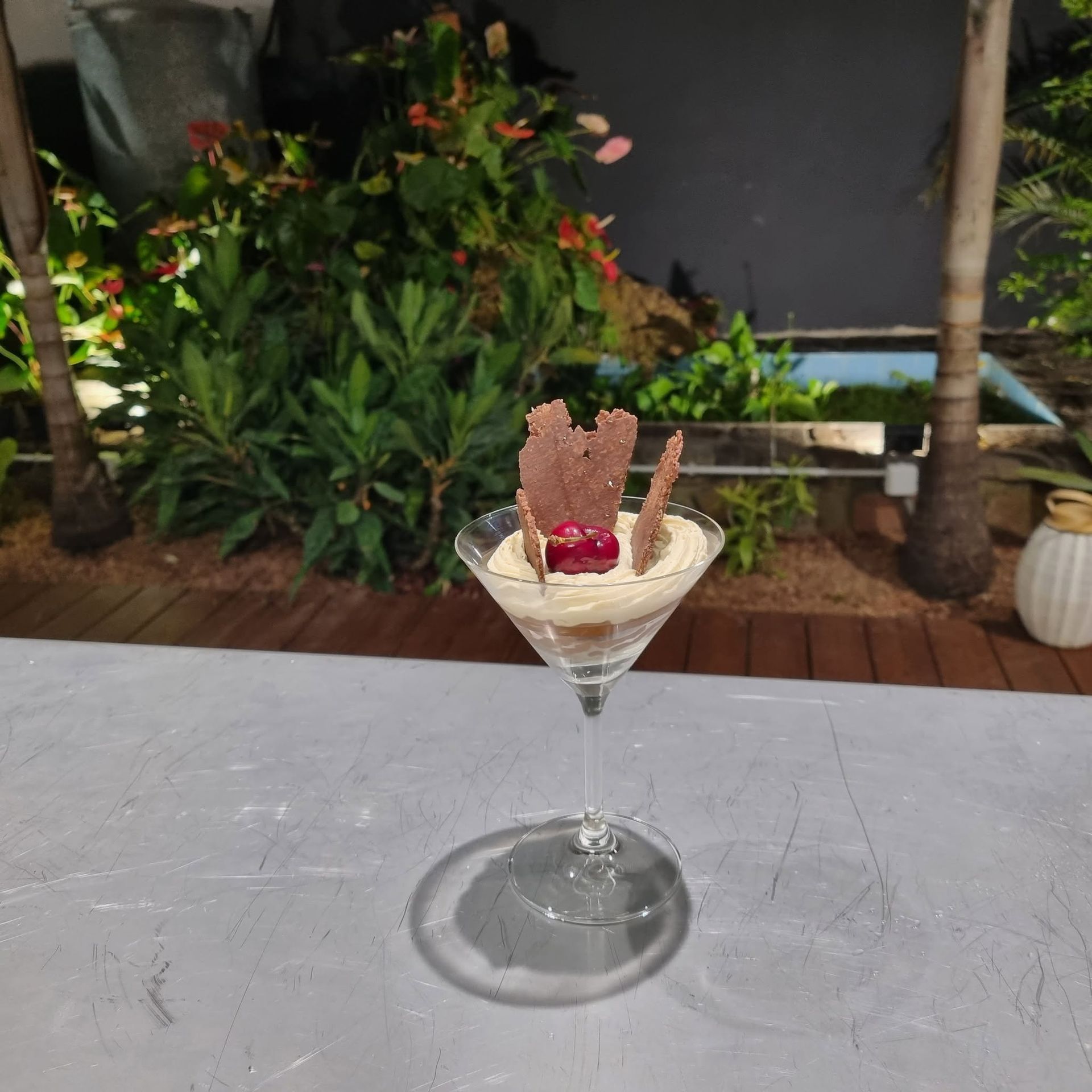 Martini dessert posé sur une table, garni d’une gaufrette et d’une baie, dans un jardin.