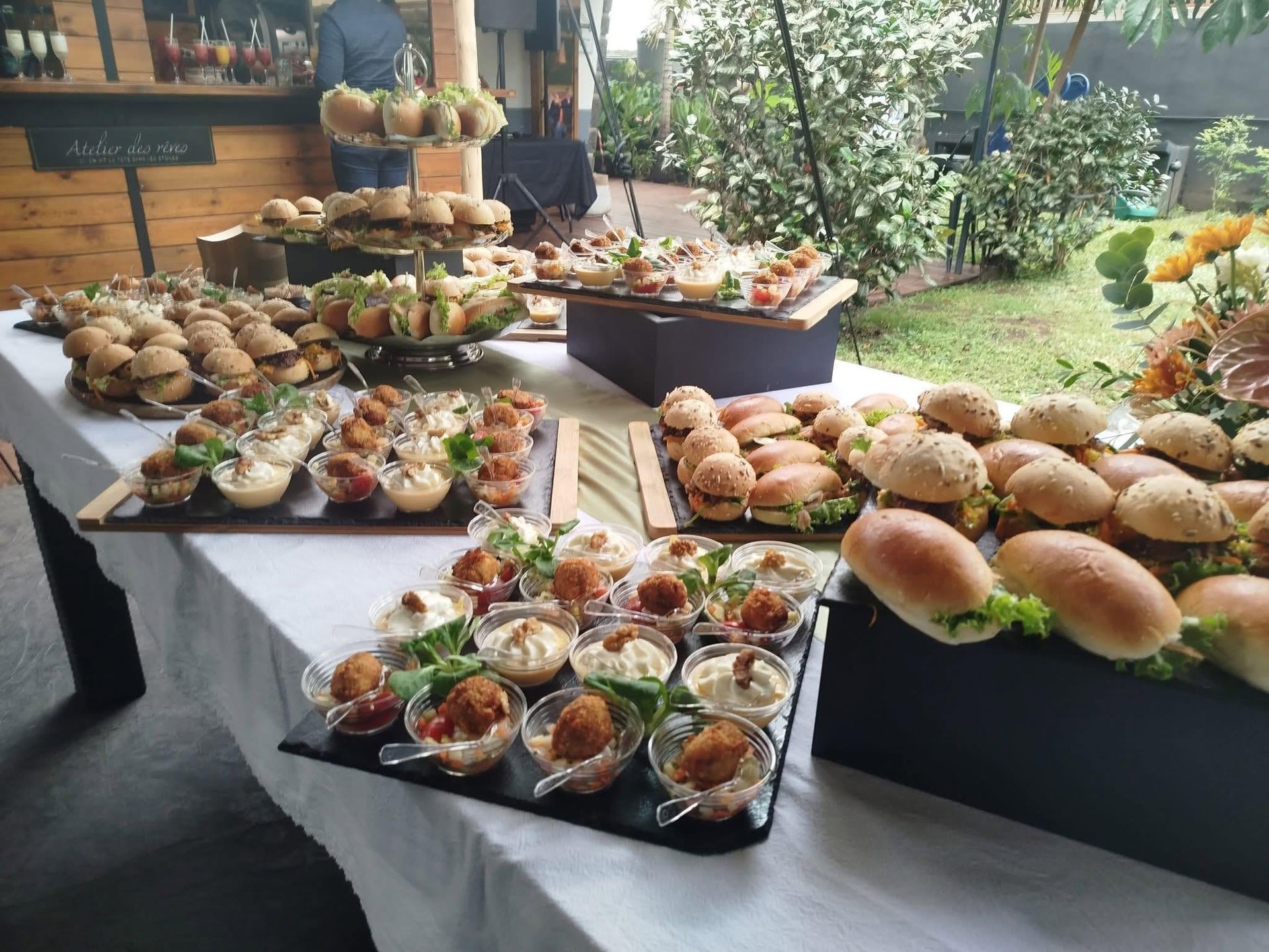 Table de buffet en plein air avec un assortiment de mini-sandwichs et d’amuse-bouches présentés sur des plateaux noirs
