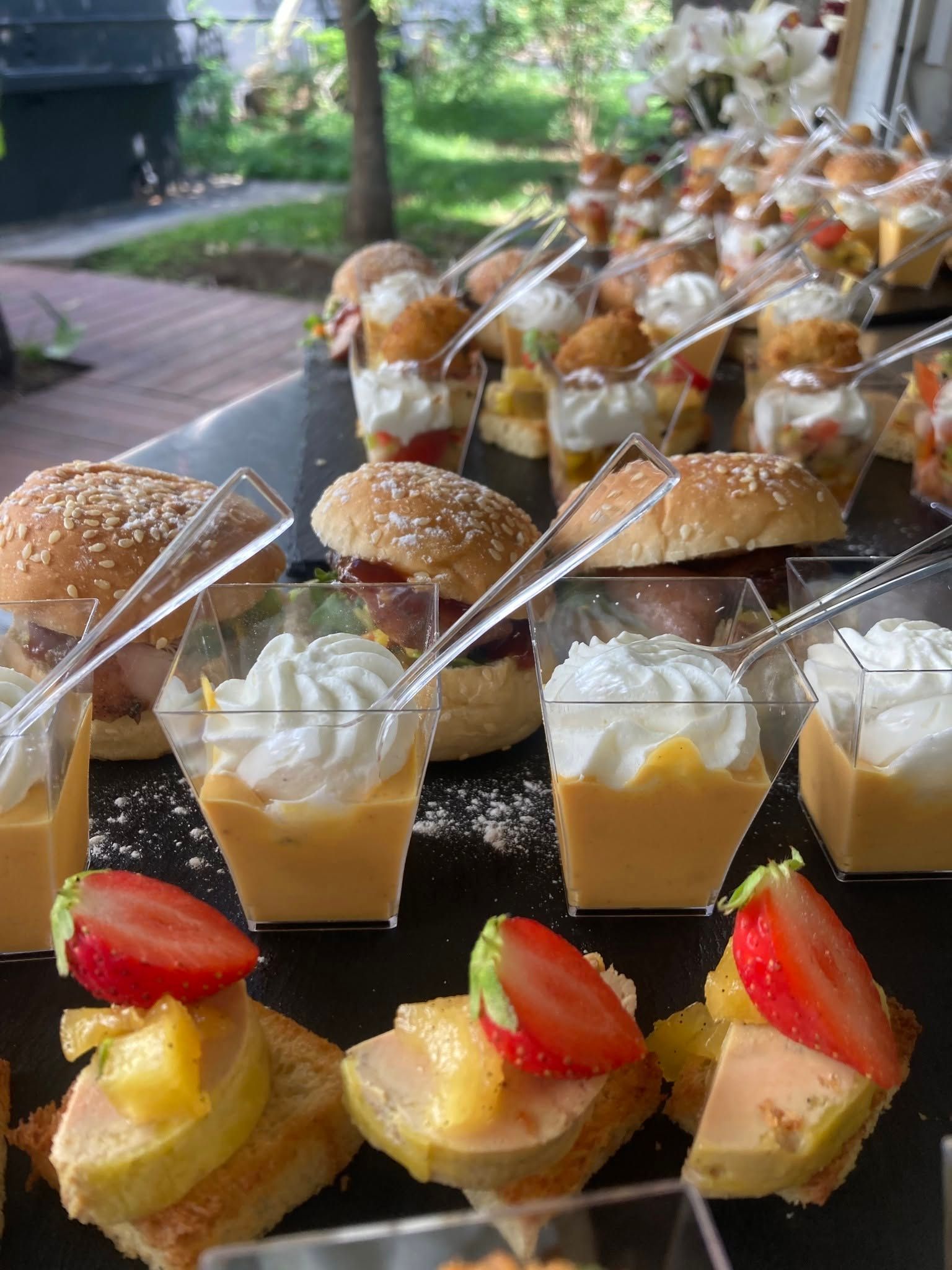 Assortiment de mini-desserts et de tartelettes disposés sur un plateau en extérieur, garnis de crème et de fraises.