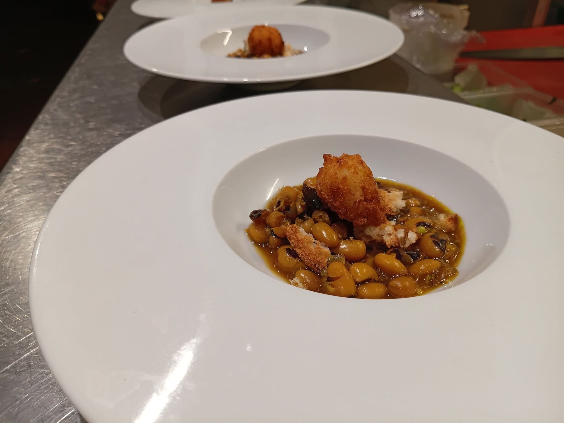 Plat raffiné dressé avec des haricots et une sauce sur une table de restaurant, avec une autre assiette en arrière-plan