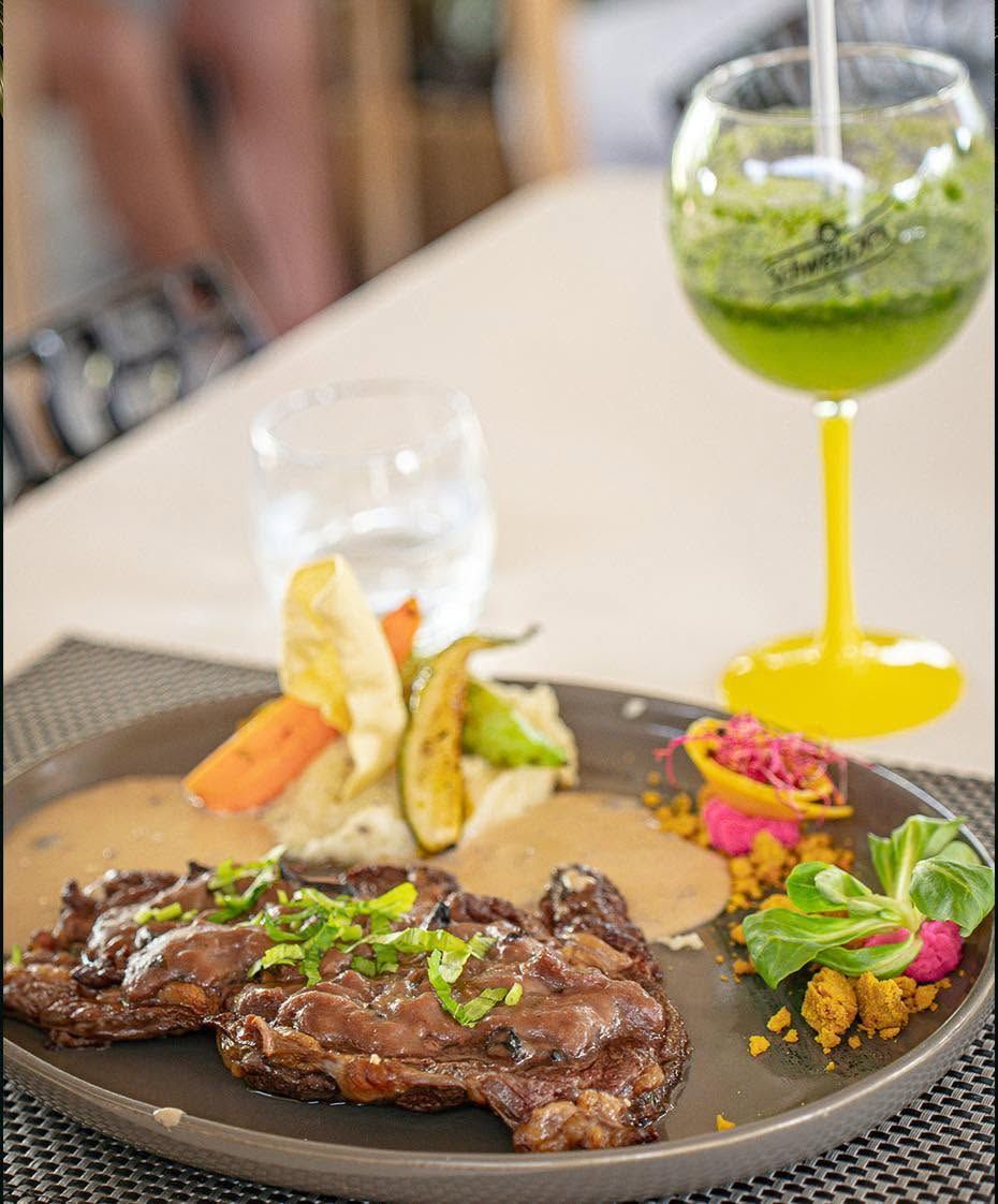Steak dressé dans une assiette avec des légumes, à côté d’un cocktail vert sur une table de restaurant