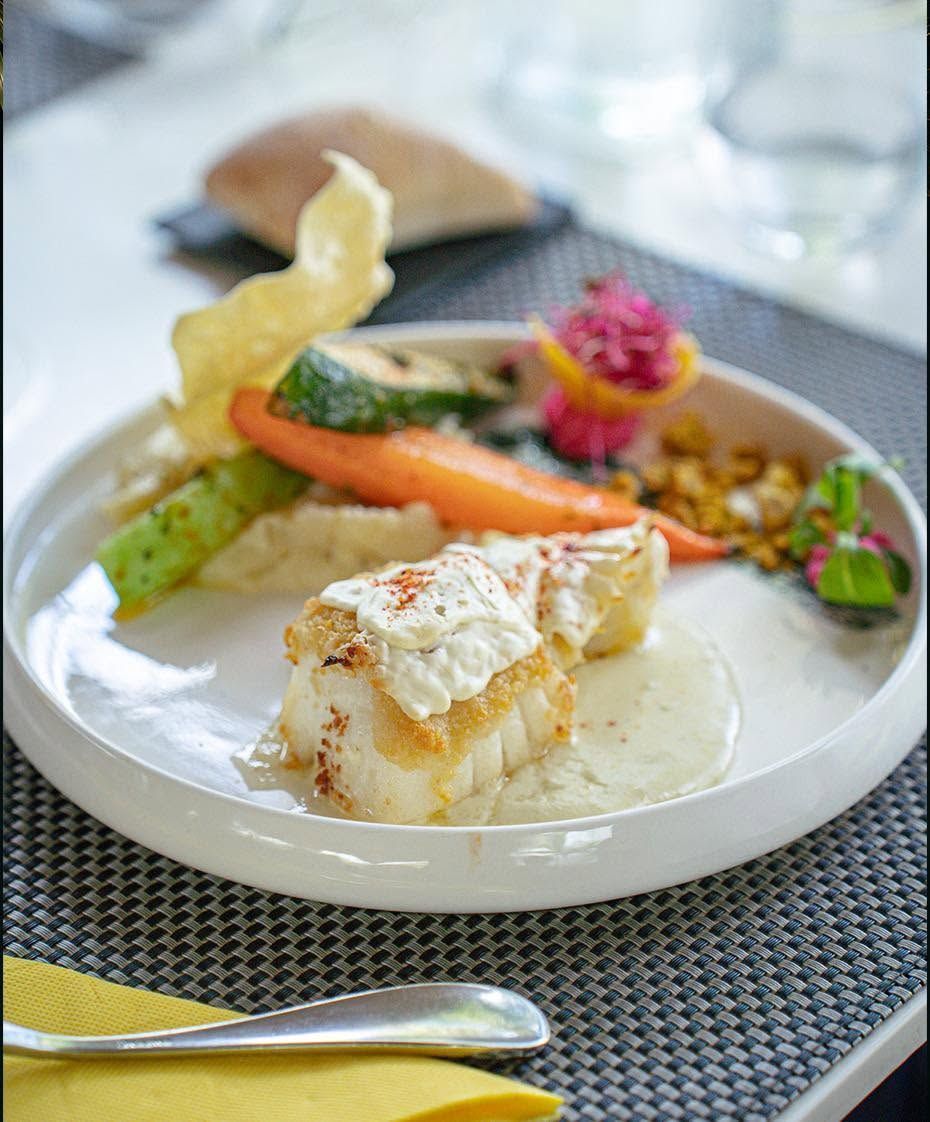 Plat gastronomique de poisson avec des légumes et une sauce, présenté sur un set de table tissé.