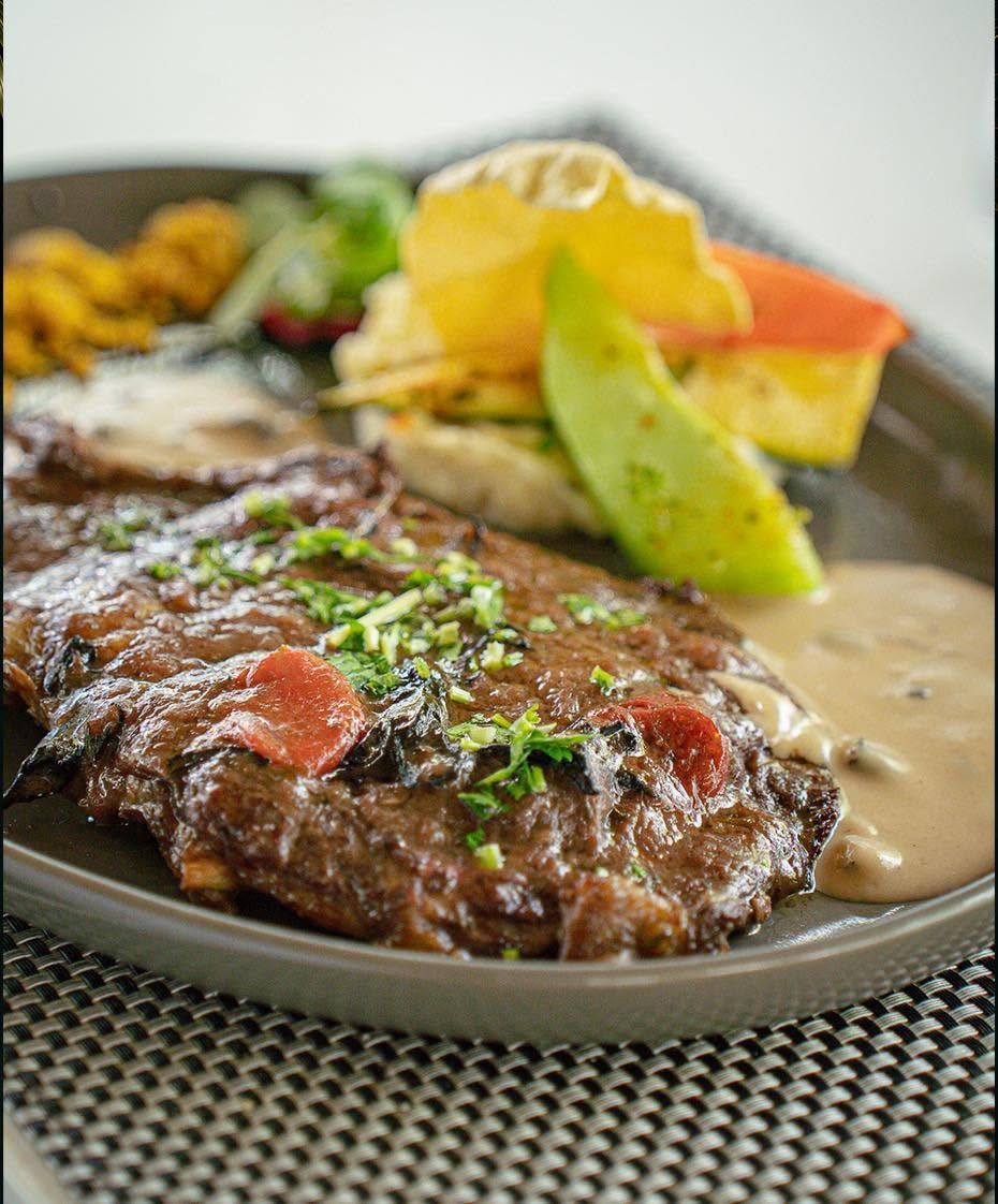 Steak grillé avec sauce, avocat et garniture, servi dans une assiette