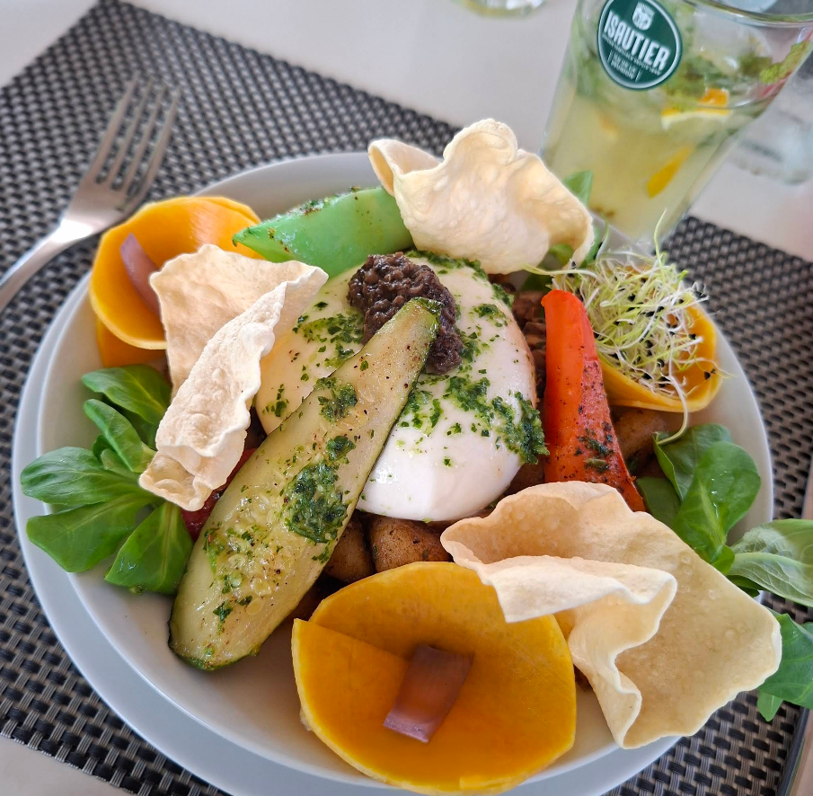 Entrée colorée de légumes dressée avec des herbes, servie dans une assiette blanche à côté d’une boisson, dans un café