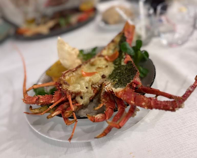 Homard grillé servi sur une assiette blanche, nappé de sauce et parsemé d’herbes, sur une table de restaurant