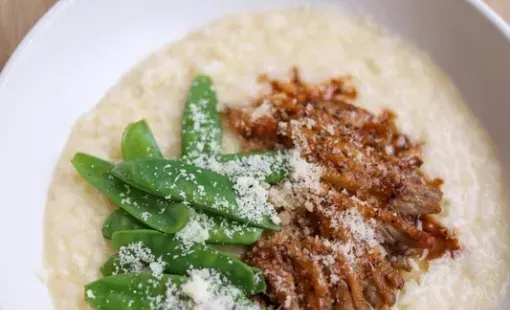 Bol de riz crémeux garni de haricots verts, d’une sauce à la viande épicée et de fromage râpé