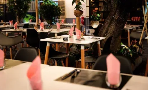 Tables vides d’un restaurant, avec des serviettes roses pliées, dans une salle de restaurant intérieure faiblement éclairée