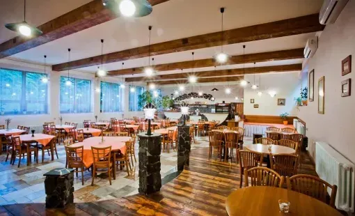 Salle de restaurant spacieuse avec des tables et des chaises en bois, des poutres apparentes et de grandes fenêtres.