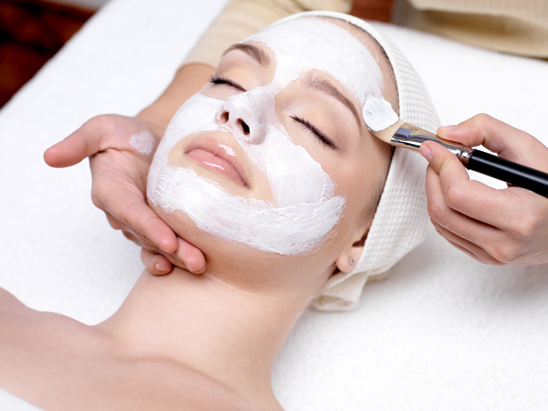 Une personne appliquant une crème sur le visage d'une femme.