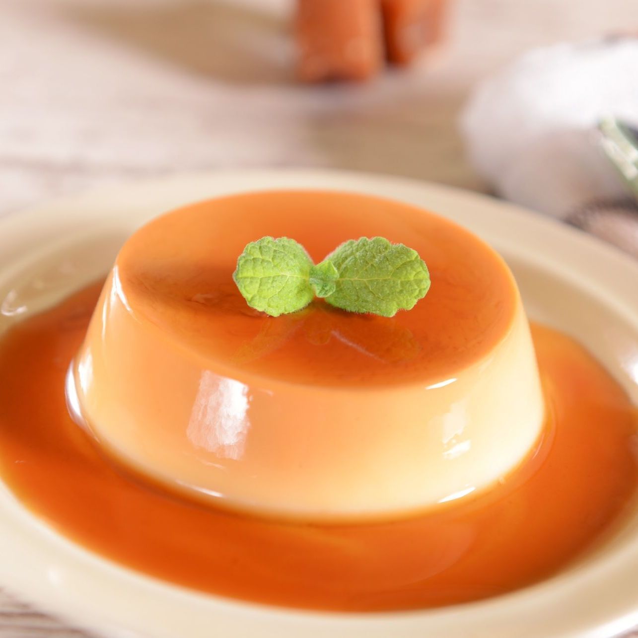 Postre de natillas de caramelo en un plato, adornado con hojas de menta, con una piscina de salsa de caramelo.