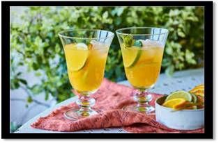 Dos vasos de bebidas de color naranja con hielo y lima, sobre una mesa con una servilleta naranja y un pequeño tazón de rodajas de lima.