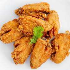 Pila de alitas de pollo fritas, crujientes y doradas, en un plato blanco, adornadas con una ramita de perejil verde.