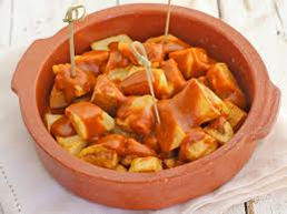 Patatas bravas en cuenco de terracota, rociadas con una salsa roja y servidas con palillos.
