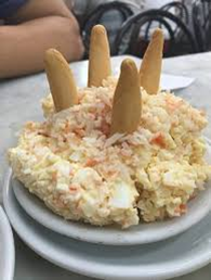 Una cremosa ensalada de patatas española, adornada con palitos de pan, servida en un plato blanco.
