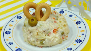 Ensalada de papa en un plato, adornada con palitos de pan y una aceituna. El plato tiene un diseño floral azul y naranja.