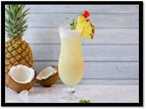 Cóctel de piña colada en copa, decorado con piña y una cereza. Cerca hay una piña y un coco.