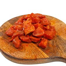 Carne cortada en cubitos, de color naranja rojizo, sobre una tabla de cortar de madera rústica.