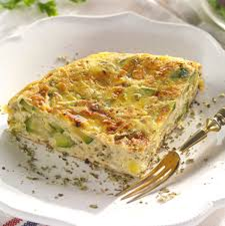 Una rodaja de frittata de calabacín en un plato blanco con un tenedor dorado, espolvoreada con hierbas.