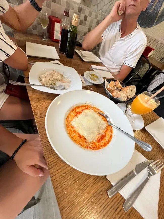 Mesa de restaurante con platos de comida, bebidas y gente. Se ven un plato de pasta con queso y un plato de arroz.