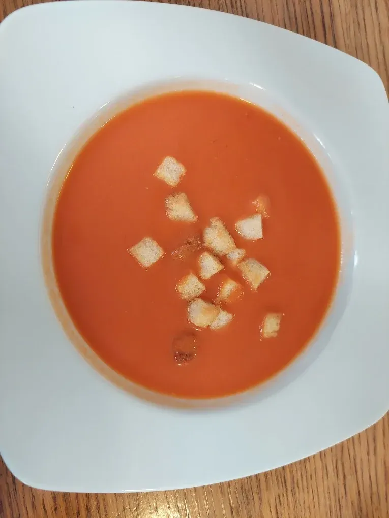 Sopa de tomate en un tazón blanco, con crutones encima. La sopa es de un rojo vibrante.